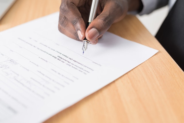 Picture of a person signing a piece of paper with a pen