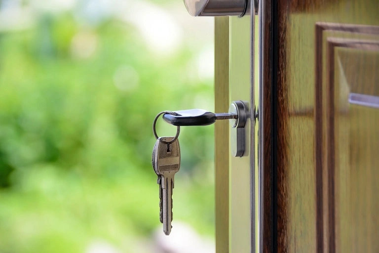 Picture of key sticking out of a lock on a wooden door.